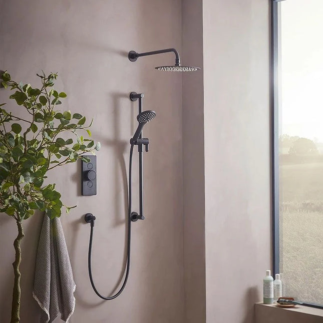 Black shower system mounted on a beige wall with a plant and window in the background.